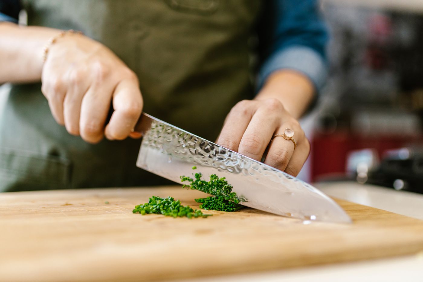 A cook chopping chives on a wooden prep board.